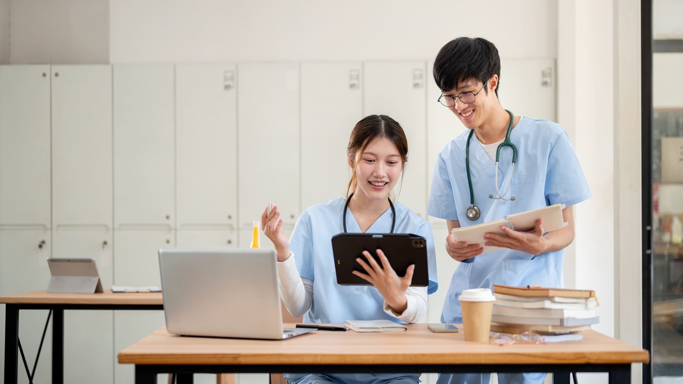 Two medical students in scrubs going through study material together on a tablet