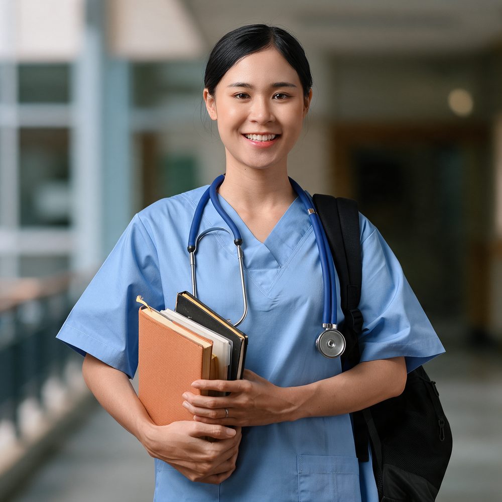 A medical student in scrubs with a stethoscope, holding textbooks in a college corridor